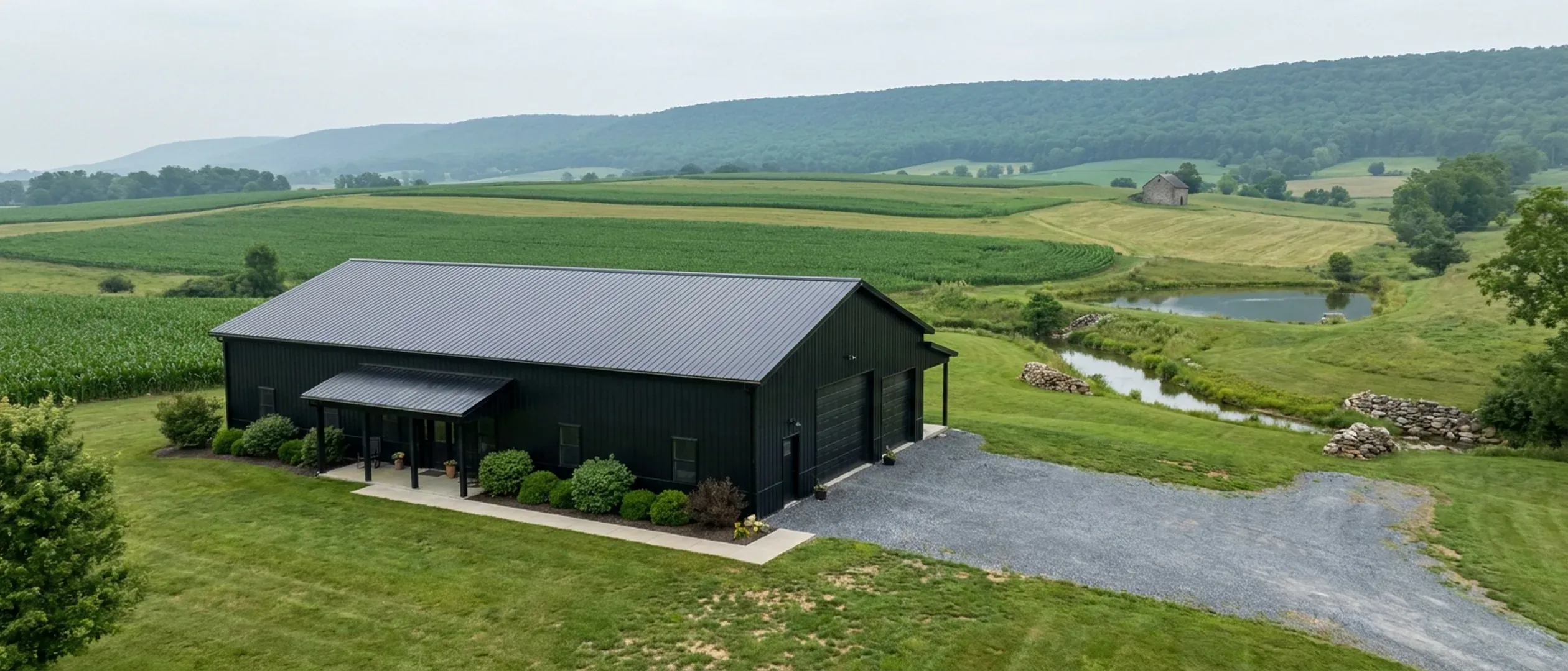 A completed barndominium with a covered entry porch and an attached shop bay, photographed in flat overcast daylight above rolling farmland.